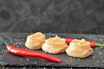Slate plate with oriental dumplings and chili pepper on dark background