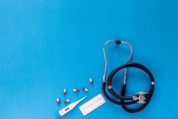 Stethoscope, colorful pills and thermometer on a blue background. Corona virus and health care concept. Copyspace and place for text and wording. Flat lay.