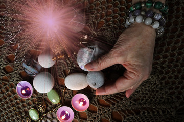 The hand of a clairvoyant lays out stones and amulets by burning candles