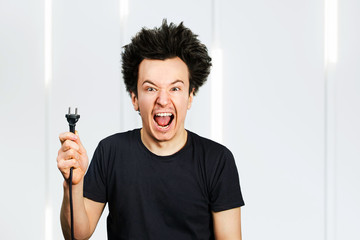 long hair guy holds an electric plug with a cable in his hand on a white background - obrazy, fototapety, plakaty
