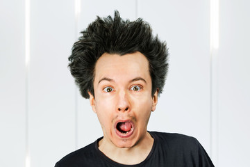 Shaggy young guy with long hair surprised with open mouth on a white background