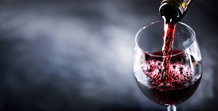 Pouring glass of red wine from a bottle in wide banner shape or copy space for text..