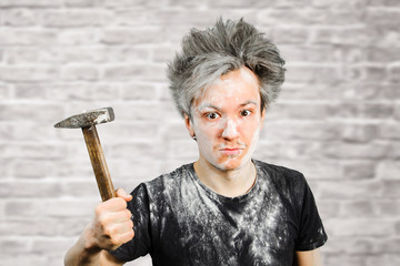 Dirty young builder guy freak in plaster is hold a hammer on brick wall background at home during...