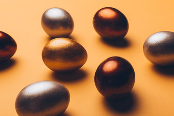 Bronze, silver and gold easter eggs on a yellow background.