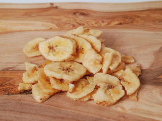 Pile of dried banana chips on a wooden board.
