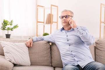 Serious mature man talking on mobile phone at home