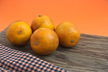 A still life with blood oranges on orange background and a wooden board