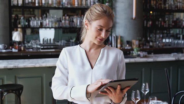 Portrait of female owner of restaurant bar standing by counter using digital tablet -  shot in slow motion