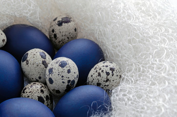 Happy easter card - place for text. Blue easter and quail eggs in a snow-white woolen cozy nest on a white wooden background, selective focus image. bright contrast blank for holiday card