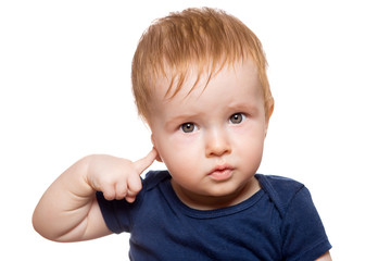 toddler with red hair in dark blue clothes looks into the frame with his eyes and holds his finger to his ear indicating a conditional sign to hear or not to listen isolated on a white background.
