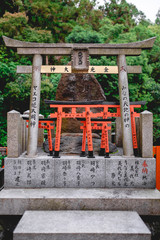 Wooden and stone torii gates and rock with kanjis at sanctuary in Fushimi Inari taisha shrine, Kyoto