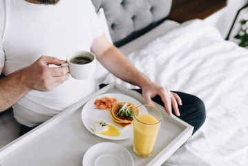 Young caucasian man eating healthy breakfast in bed on tray
