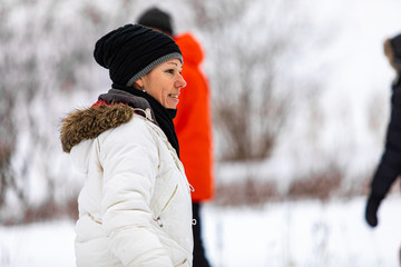 A smiling woman who is outdoors in winter with some people. A laughing woman in a white jacket and black hat on camping with her friends