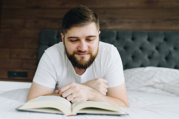 Close up young handsome caucasian man reading a book lying in bed