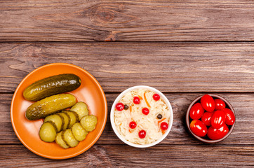 Homemade tasty fermented milk products on plates - sauerkraut, tomatoes, pickles, on wooden background, copy space.