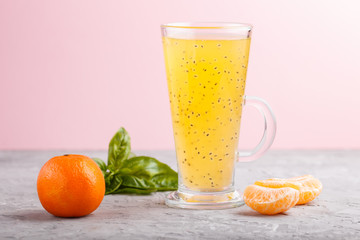 Glass of tangerine orange colored drink with basil seeds on a gray and pink background. Side view
