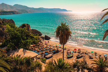 Nerja, Málaga. Sunny view of the Mediterranean Sea from Costa del Sol. With clean water, people at the sand and giant palm trees. - obrazy, fototapety, plakaty