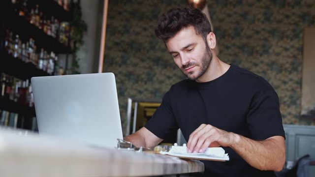 Male owner of restaurant sitting at bar counter with laptop working  - shot in slow motion