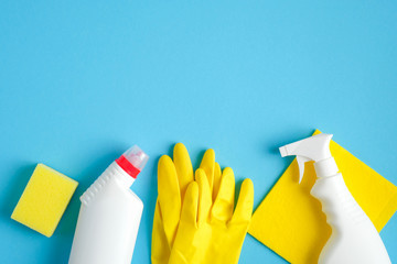 Cleaning supplies on blue background. Top view cleaner spray bottle, rag, yellow sponge, detergent, rubber gloves. House cleaning service and housekeeping concept