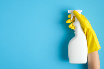 Hand in a yellow rubber glove holds cleaner spray bottle over blue background. Cleaning service banner mockup. Housecleaning and housekeeping concept. Flat lay, top view - obrazy, fototapety, plakaty