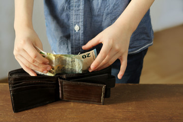 kid holds euro banknotes in his hand and puts them in a brown wallet, concept of pocket money,...