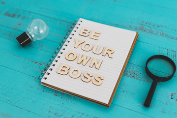 being a business owner, notebook on desk with Be your own boss text surrounded by lightbulbs symbol of good ideas