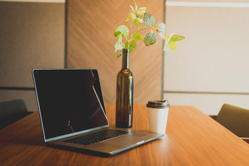 Laptop and cup of take away coffee on a table. Lifestyle concept. Mockup for coffee brand. Green template on laptop