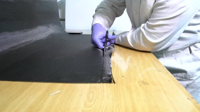 Worker Specialist in composite with white coat and gloves, cuts carbon fiber using special scissors, in the workshop.
