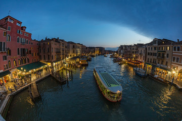 VENICE, ITALY - August 02, 2019: View from Rialto Bridge in Venice at sunset time. Venetian Grand Canal with historical buildings, hotels, tourist boats, piles, berths. Fish eye lens shot