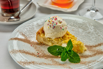 Piece of cake charlotte with apples ice cream ball and fresh mint on white plate. Served with a rosette of honey, a cup of aromatic tea and a glass of white wine