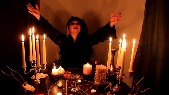 Female Fortuneteller divines in a dark room, candles are burning on a round esoteric table with a pentagram, animal skulls lie, the concept of magic, witchcraft