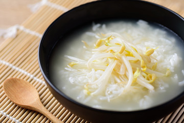 Rice soup with mung bean sprouts in a bowl and wooden spoon on bamboo sheet, Asian vegan food