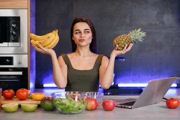 Woman choosing between dessert and fruits at table in kitchen. Healthy diet