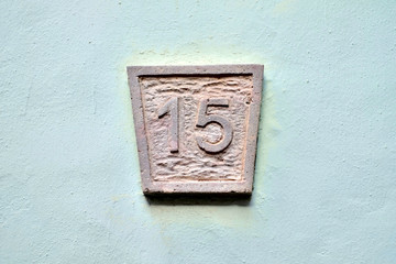 Number 15, fifteen, stone relief plate on a pastel green wall.
