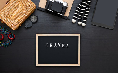 summer travel flat lay of traveller accessories set.blackboard,hat,yellow wicker bag,camera on black wooden table of influencer