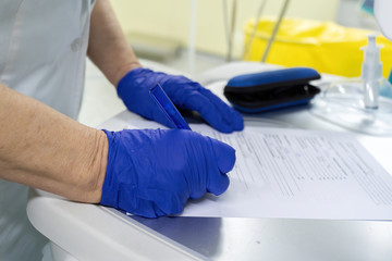 A doctor in sterile blue rubber gloves writes pen data on the indicators of devices in a special document. Operating room. Hospital and doctors. Saving the life of the patient.