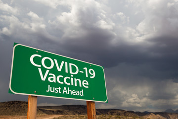 COVID-19 Coronavirus Vaccine Green Road Sign Against Ominous Stormy Cloudy Sky