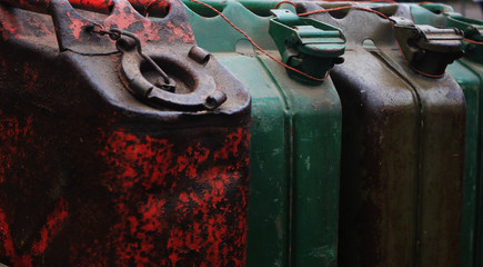 A few large, old metal cans  to fill with fuel lined up next to eachother full of rest and in red,...