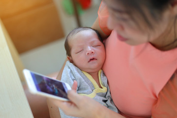 mother playing mobile phone in business home office with cute baby newborn sleeping