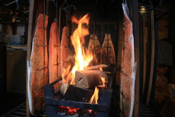 Slices of salmon being smoked/cooked on a fire with a traditional method using wooden plates to keep the salmon up