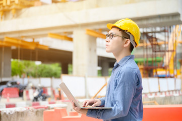 Young asian engineers are working on the construction site. Wear a yellow helmet safety. Hand holding computer laptop