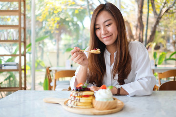 A beautiful asian woman eating ice cream with a mixed berries pancakes and whipped cream by wooden spoon