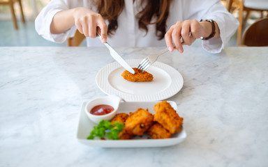 Closeup image of a woman using knife and fork to eat fried chicken in restauran