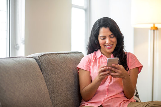 Smiling Hispanic woman using her phone at home.
