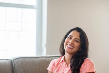 Young Hispanic woman smiling sitting on a sofa.