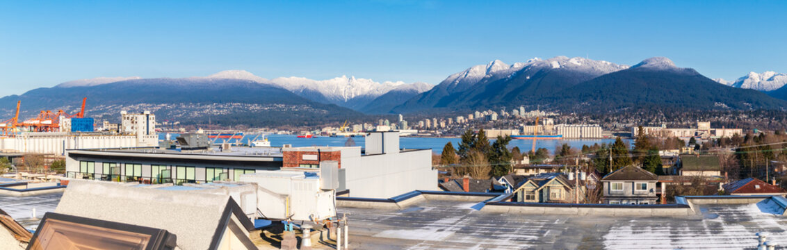 North Vancouver and West Vancouver winter panorama from Vancouver rooftop, BC, Canada. Snow capped mountains: Lions, Grouse Mountain, Fromme. Vancouver Harbour: industry, tanker and tug boats.