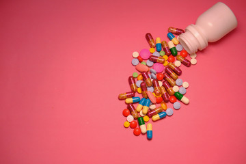 Close up of colorful pills spilling on pink background 