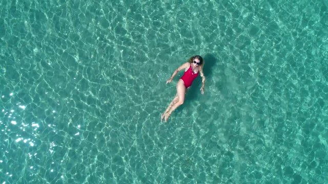 Top view of young pretty sexy girl in red swimsuit floating on water surface in crystal clear turquoise ocean. Happy island lifestyle. Vacation at Paradise. Ocean relax, travel to Philippines