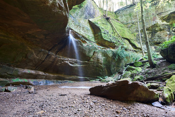 A waterfall cascading over a rock ledge in Hocking Hills. It is a lush summer, with most a ferns thriving nearby.