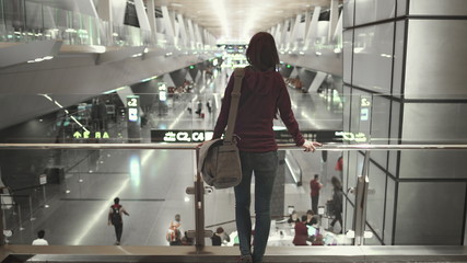 Woman Passenger Stand Look at Modern Airport Hall. Camera Pan to Caucasian Girl with Shoulder Bag. Busy International Terminal. Boarding Gate Sign, People Rush Rack Focus.